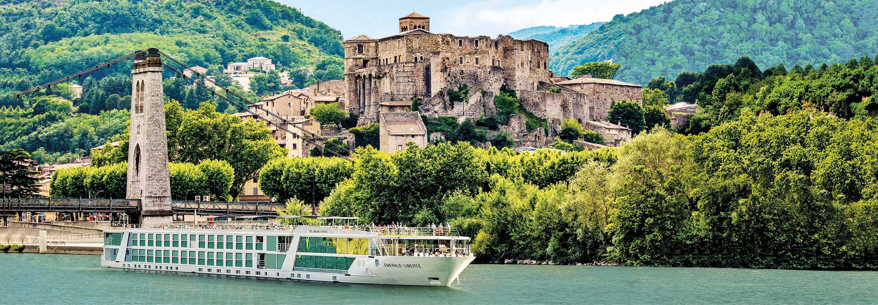 Emerald Cruises Star-Ship, Emerald Liberte cruising down the river in France with a fortress and lush green trees in the background