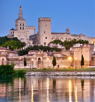 Fortress building lit up at dusk, reflecting on the water of the Rhone river