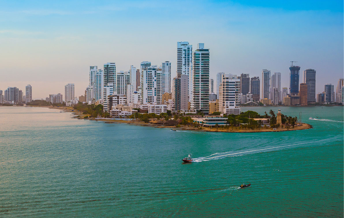 View of the Colombia skyline, with many tall buildings, and with people boating in the azure sea next to the city.