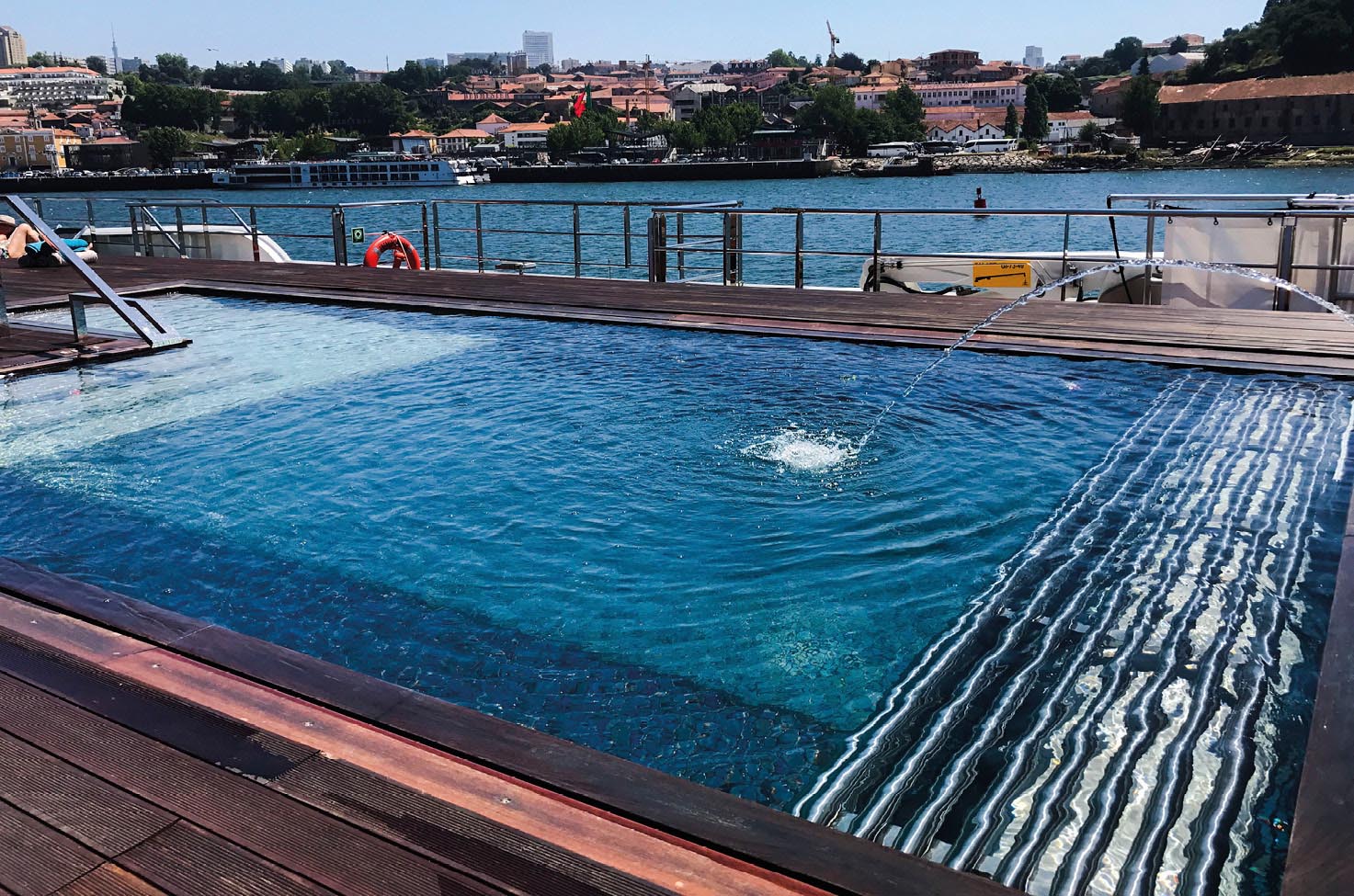 A view of the Serenity Pool found on the Emerald Radiance Star-Ship. A spacious blue pool is seen on an open deck with views of the Portuguese landscape in the background.