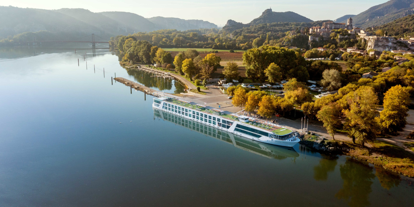 Emerald Ship can be seen docked by a bank. The trees in the background are a mix of green and yellow.