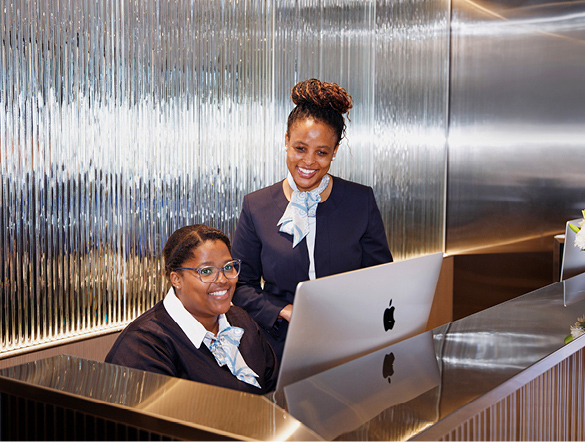 two receptionists smiling wearing smart attire looking at a computer screen