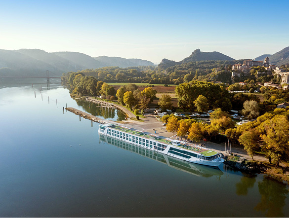 River cruise ship docked in Viviers, France, near trees and with rolling hills visible through the light mist