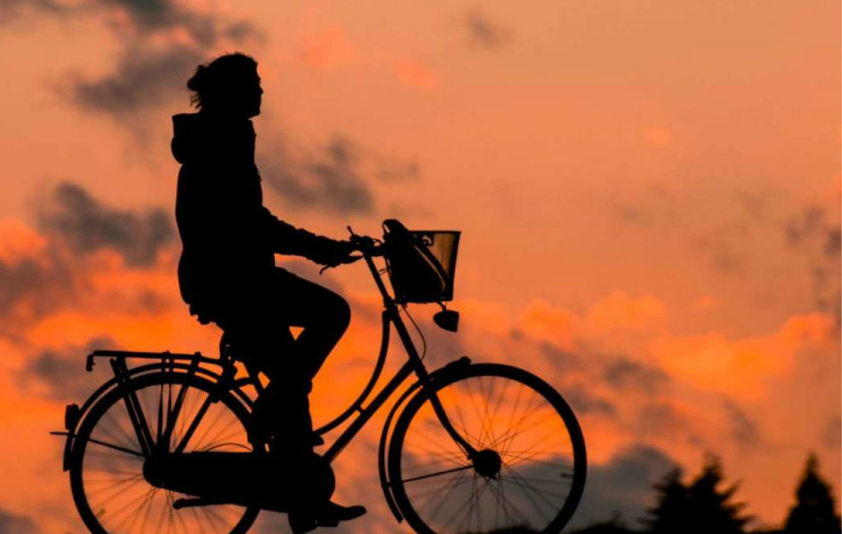 The silhouette of a person seen cycling set against an orange sky.
