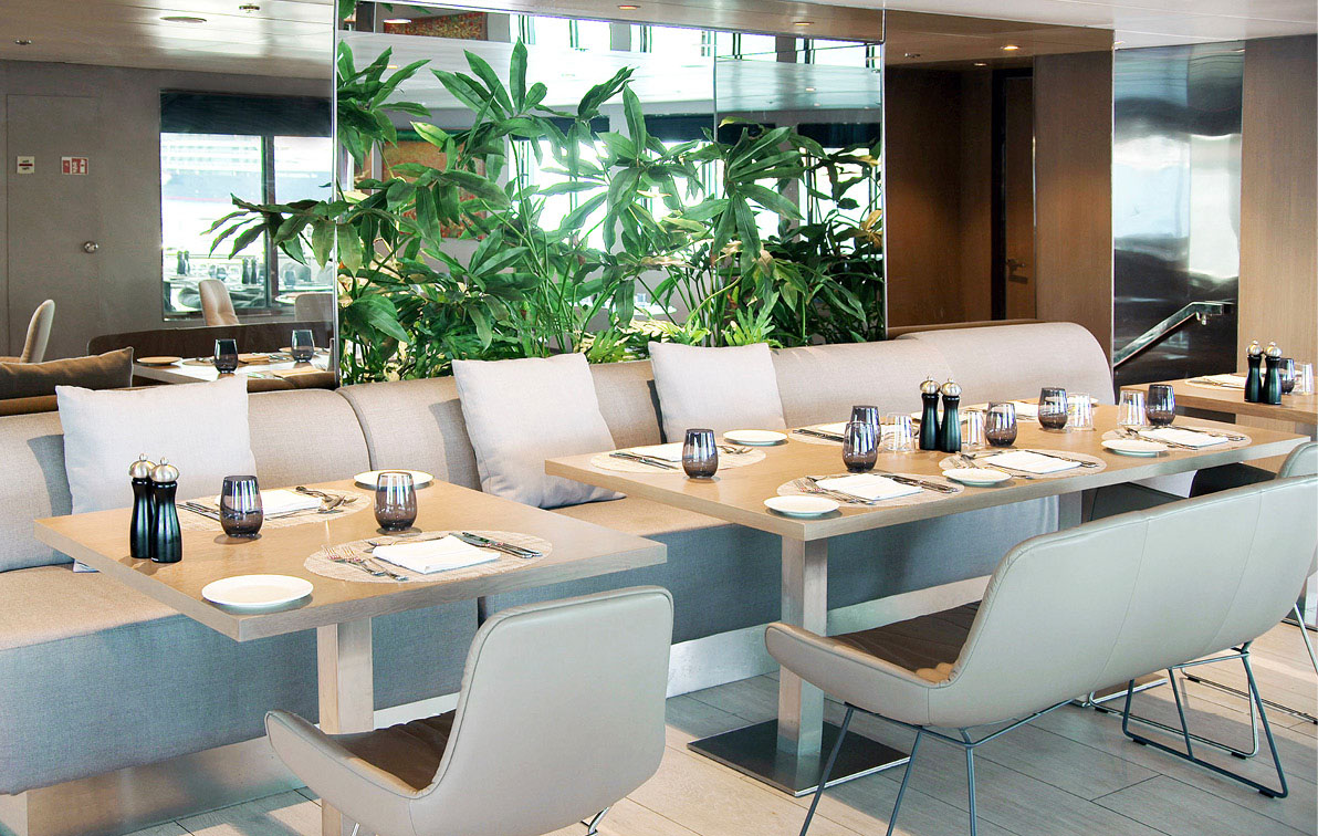 Dining area set up on board a luxury yacht cruise. A bright and airy space with mirrors and plants give a splash of colour.