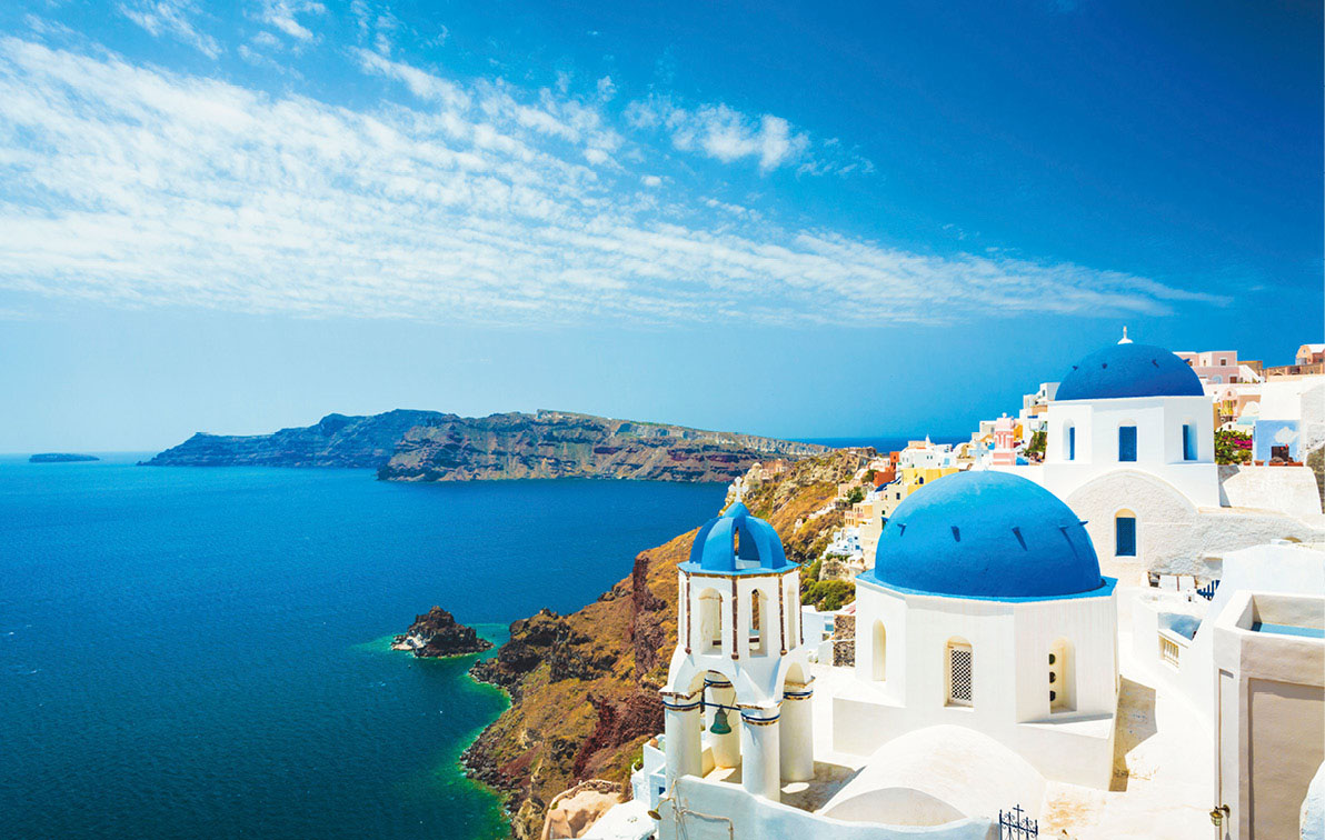 Blue-domed church of Santorini, Greece on a bright sunny day, with light cloudy sky and deep blue sea